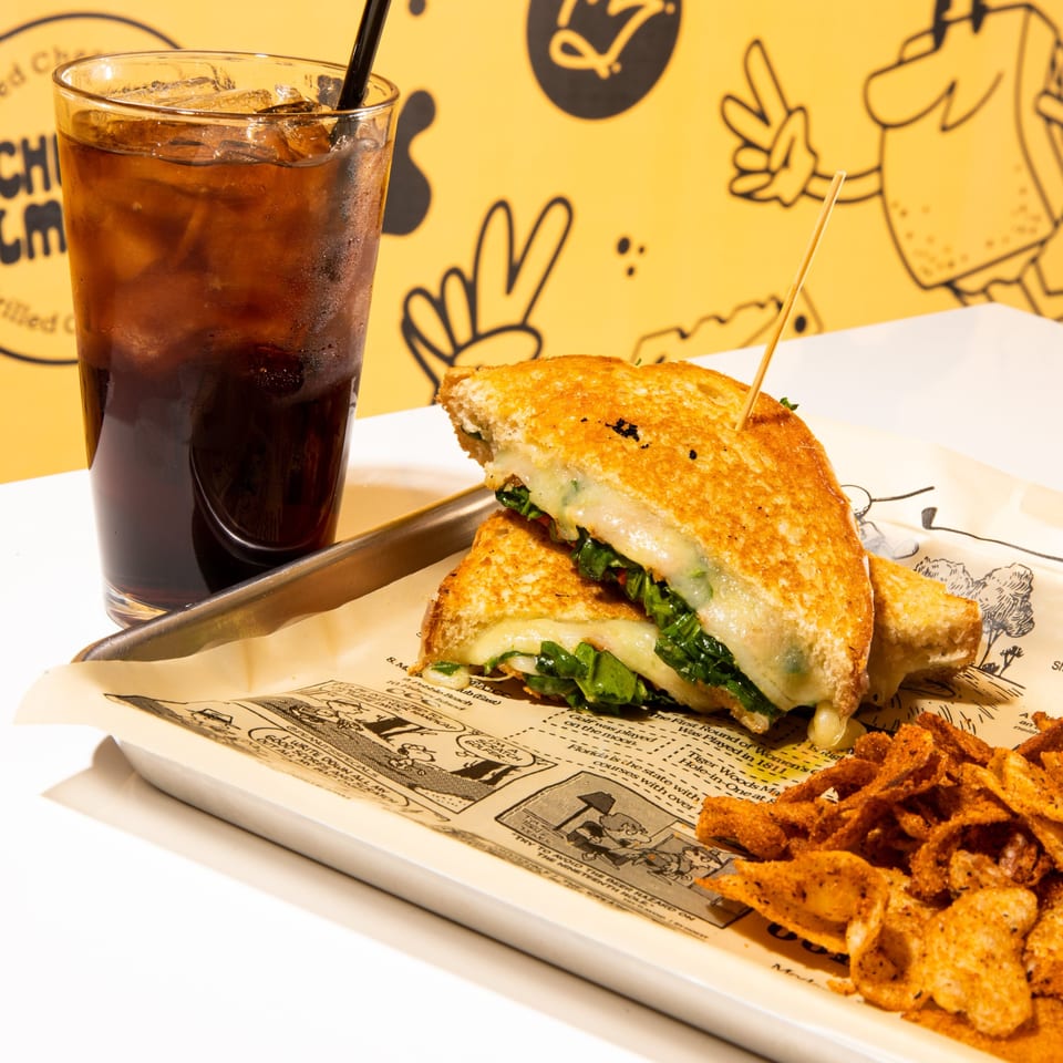 A Cheese Almighty grilled cheese sandwich with chips and a drink on a tray.