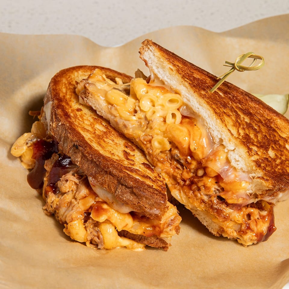 A grilled cheese sandwich from Cheese Almighty, filled with macaroni and cheese and pulled pork, on brown paper.