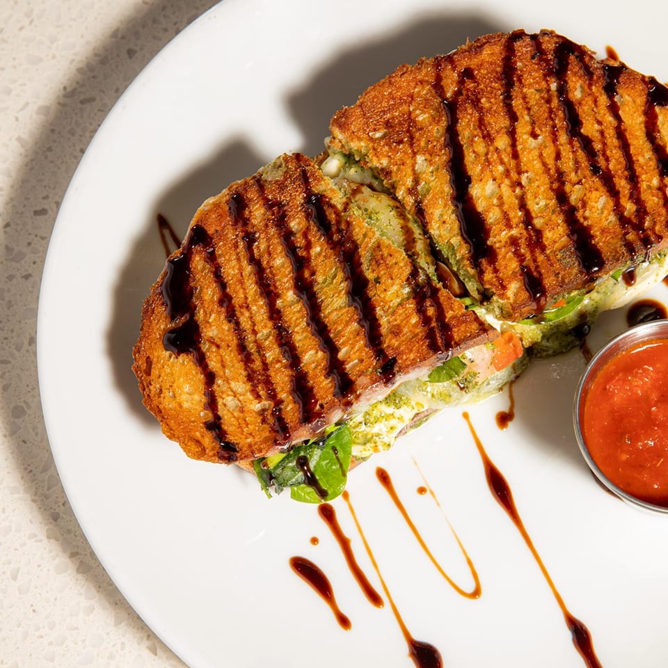 Grilled cheese sandwich with pesto, tomatoes, and balsamic glaze, served with a side of marinara.