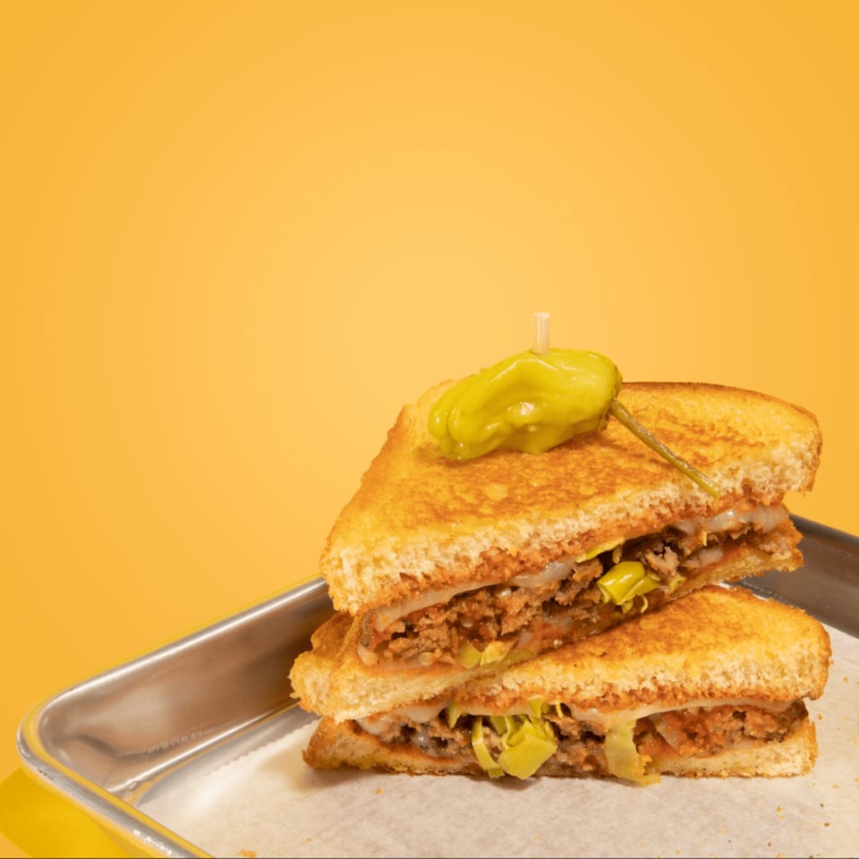 A grilled cheese sandwich from Cheese Almighty, cut in half and stacked, with a pepperoncini on top.