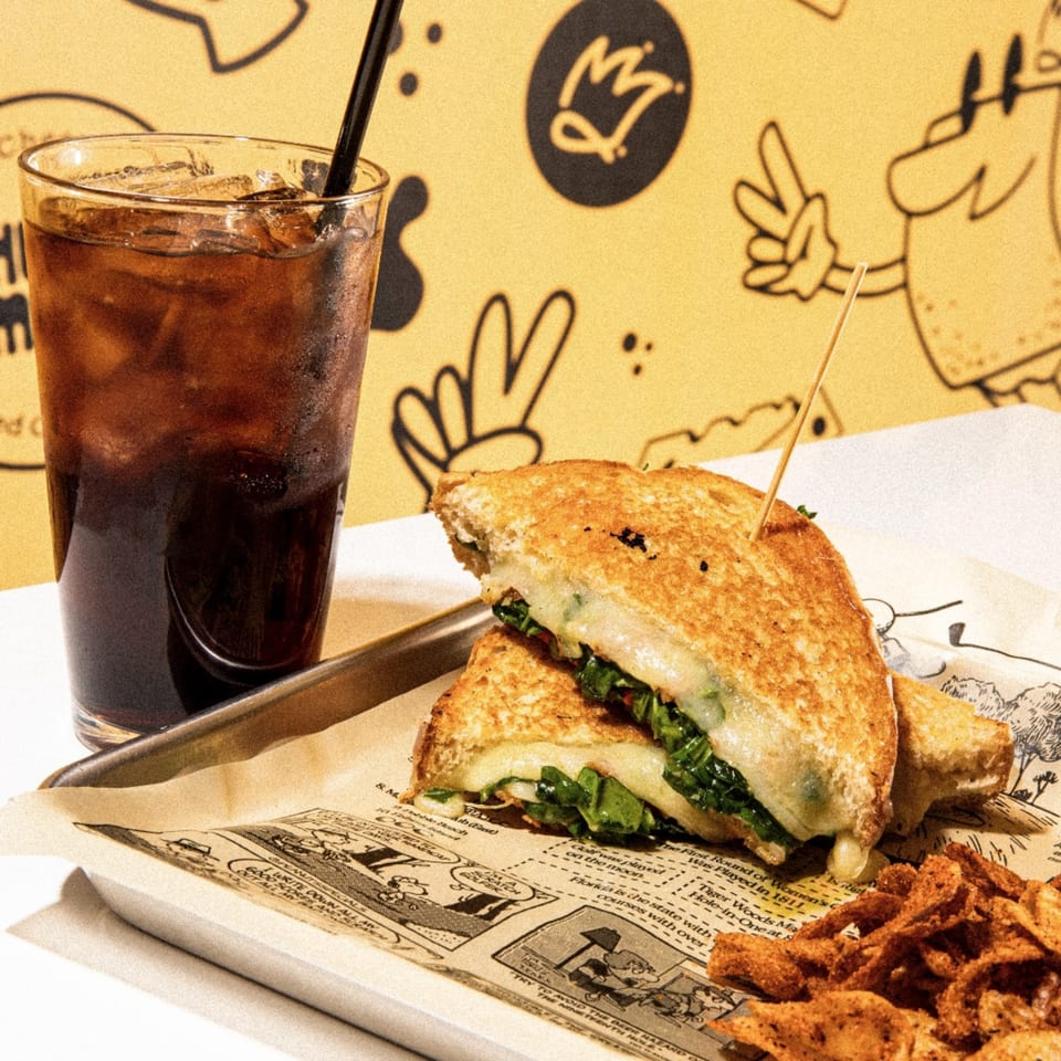 A grilled cheese sandwich with greens, a side of chips, and a soda on a tray.